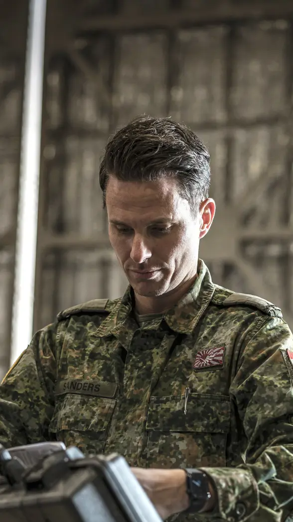 Een militair in een groen camouflagepak bekijkt een koffer die hij uit een container pakt.