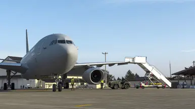 Een groene tow truck rijdt met een grote vliegtuigtrap naar een A330 MRRT die links in beeld staat.