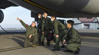 Een groep Japanse militairen knielt en staat gebogen onder de romp van een A330 MRTT en kijkt en wijst naar boven.