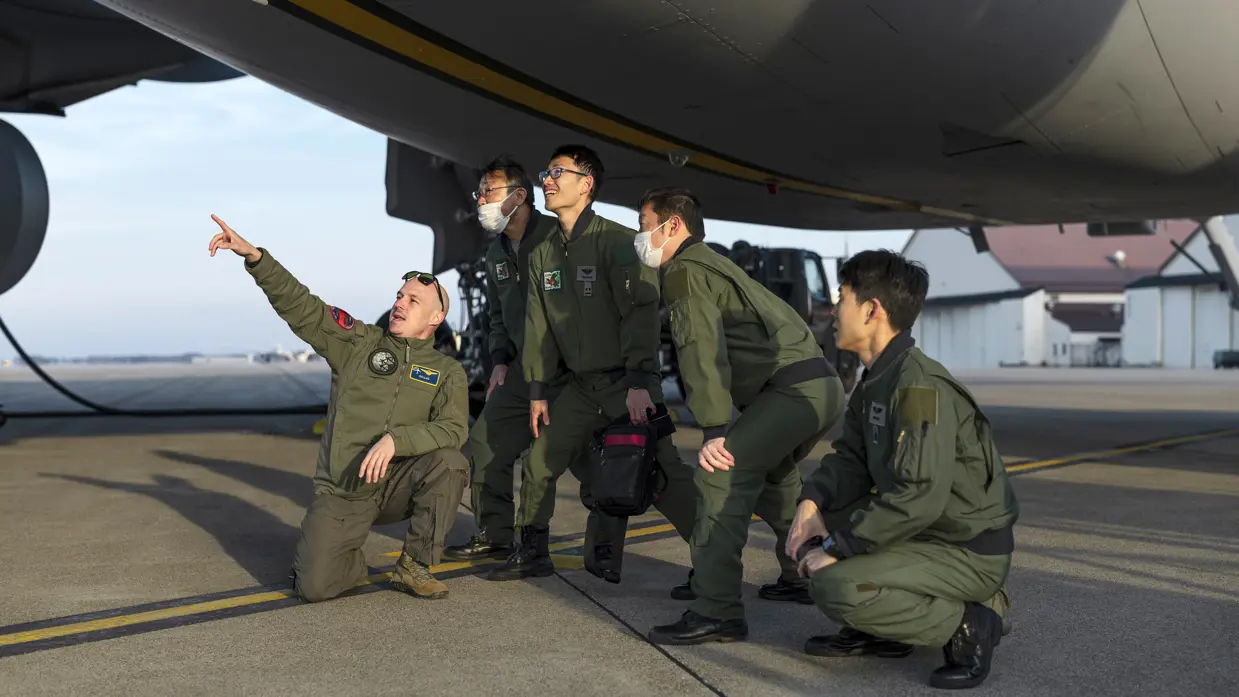 Een groep Japanse militairen knielt en staat gebogen onder de romp van een A330 MRTT en kijkt en wijst naar boven.