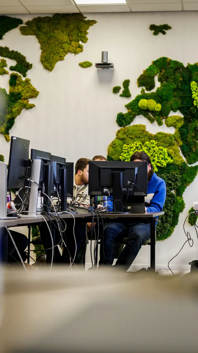 Werkende mensen achter computers met een wereldkaart van mos op de achtergrond. 