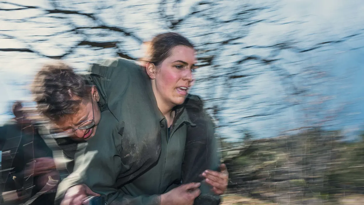 Een vrouwelijke militair rent met een bebrilde mannelijke collega in de brandweergreep.