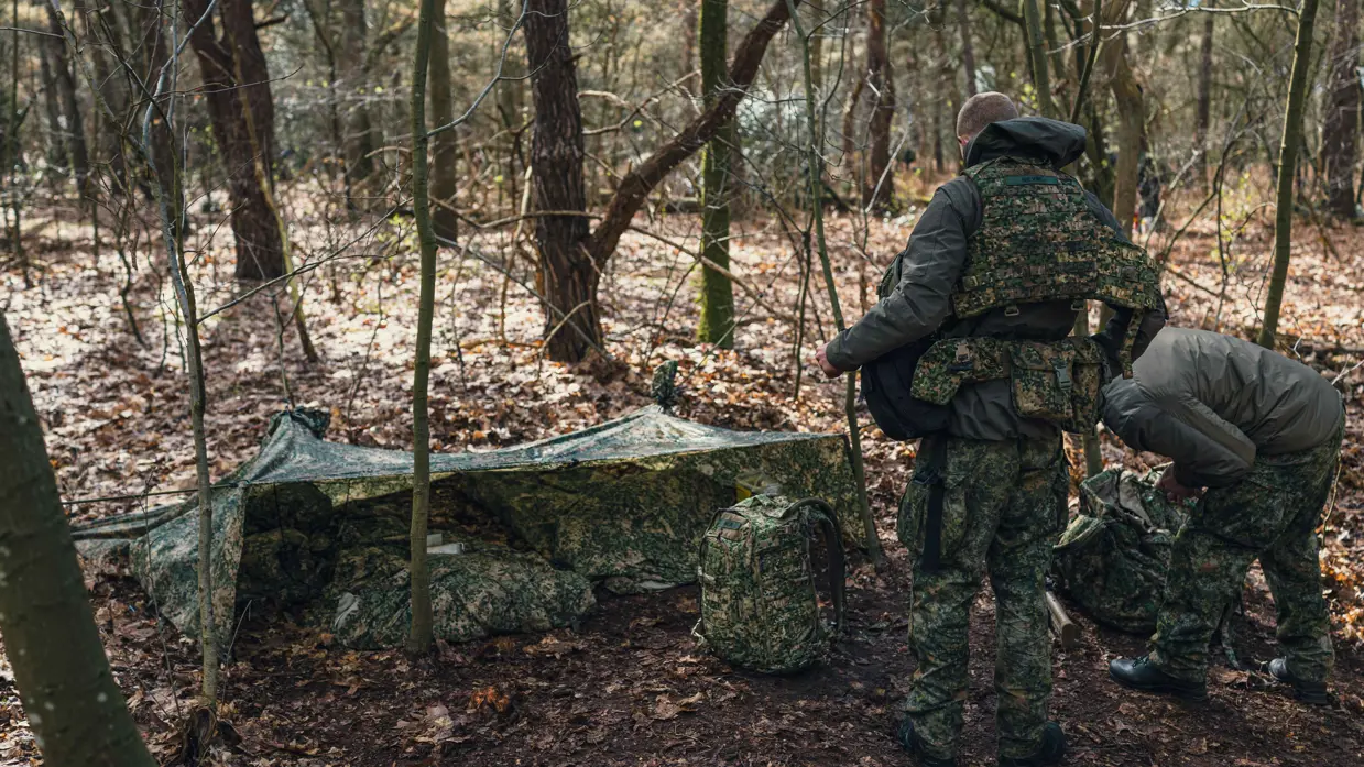 2 militairen ontfermen zich over 2 rugzakken voor een camouflagetentje.