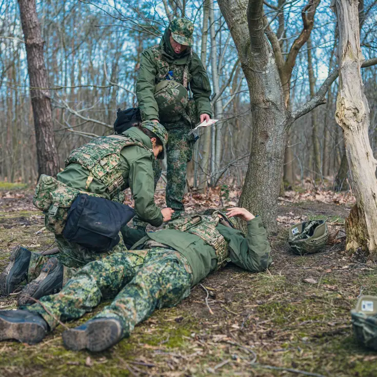 2 militairen ontfermen zich over een gewonde collega op de grond.