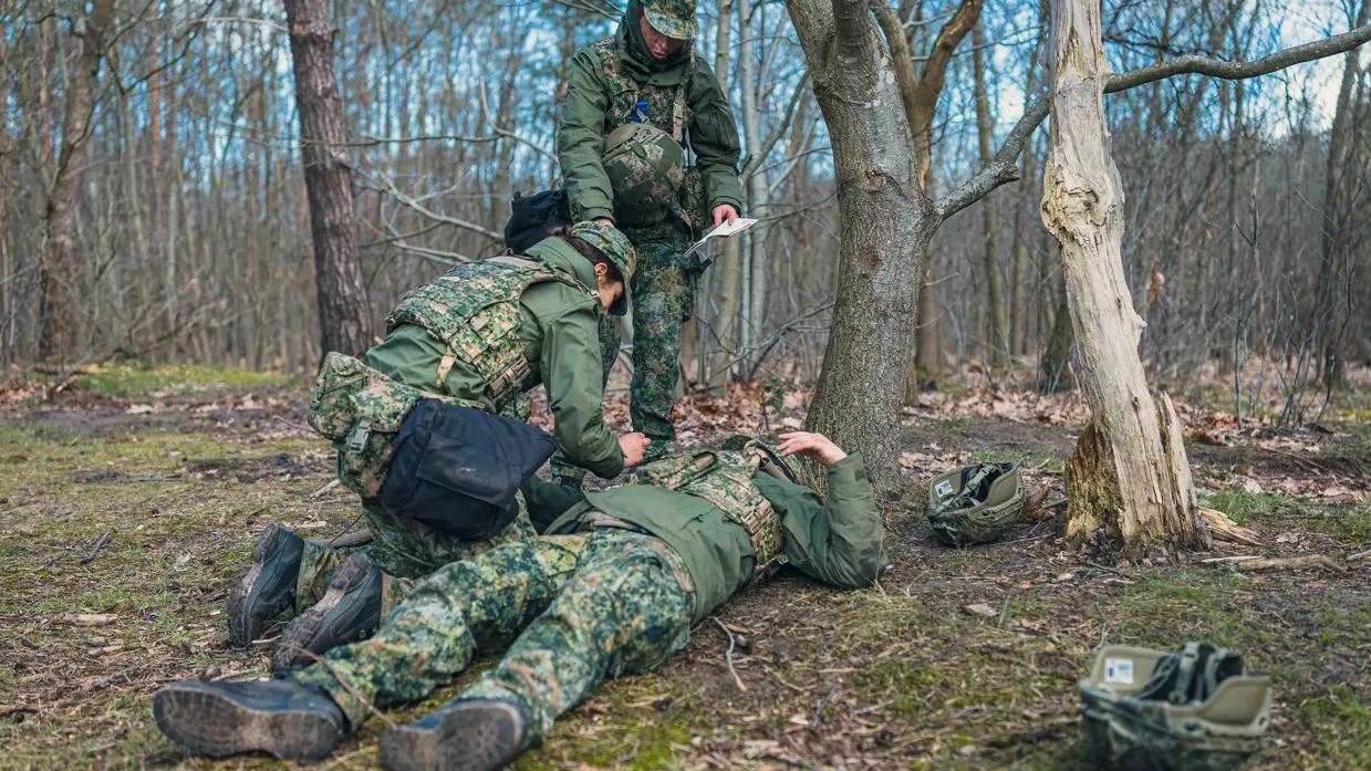 2 militairen ontfermen zich over een gewonde collega op de grond.
