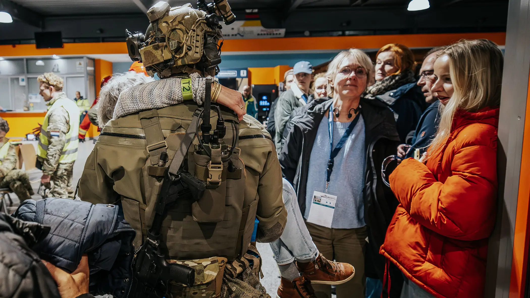 Een operator van NLMARSOF draagt een vrouw in zijn armen. Hij loopt een terminal binnen waar ook andere passagiers worden opgevangen.