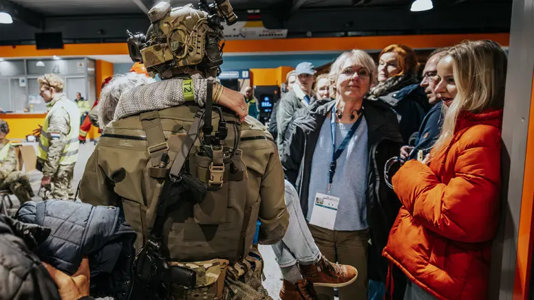 Een operator van NLMARSOF draagt een vrouw in zijn armen. Hij loopt een terminal binnen waar ook andere passagiers worden opgevangen.