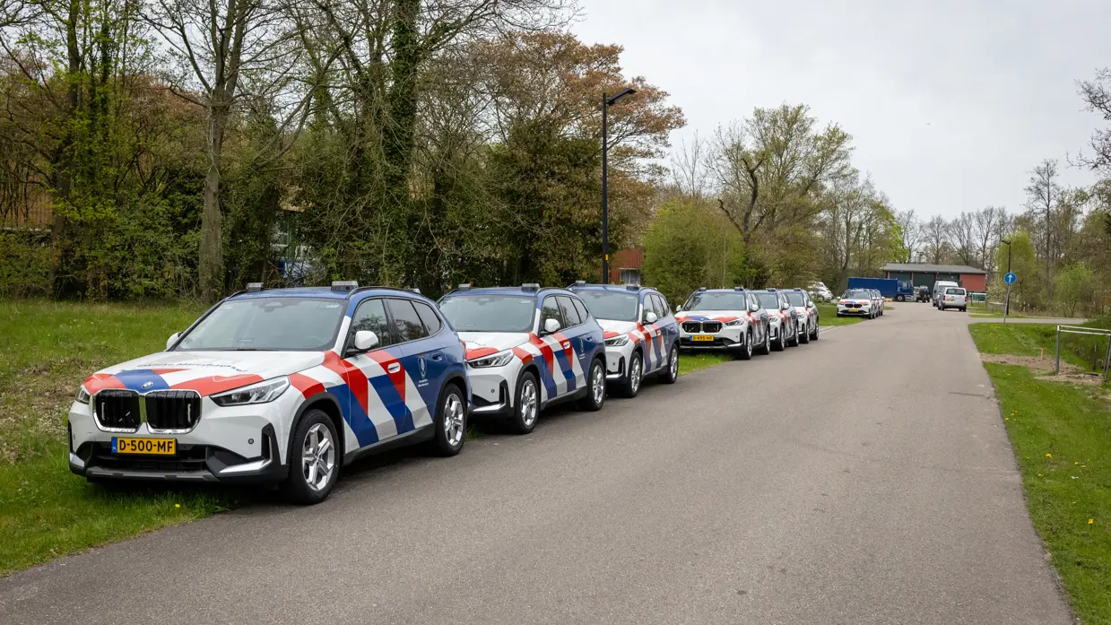 Voertuigen Marechaussee staan achter elkaar in de berm geparkeerd.