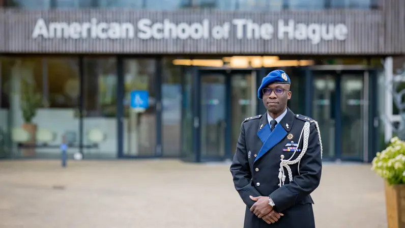 Marechaussee in uniform staat voor ingang schoolgebouw.