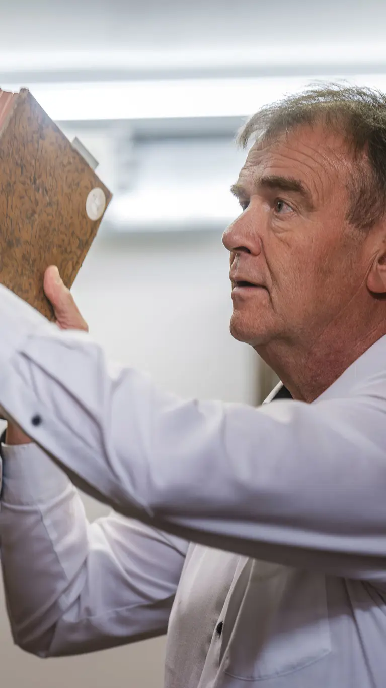 Een man in een wit overhemd pakt een oud, bruin boek van een plank vol oude boeken in een bibliotheek.
