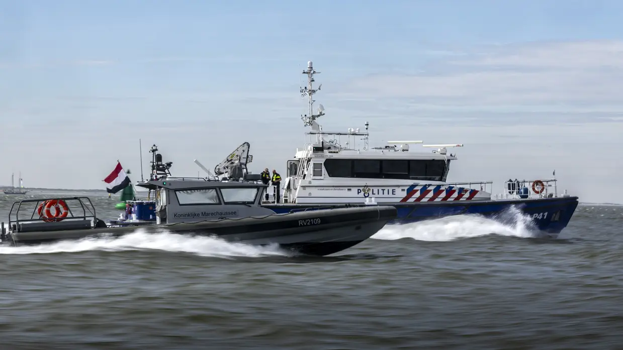 Een politieboot en een rhib-boot van de Koninklijke Marechaussee varen zij aan zij.