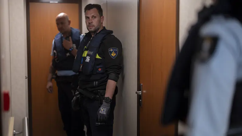 Een marechaussee en een politieman staan in een hal tegenover aan andere marechaussee.