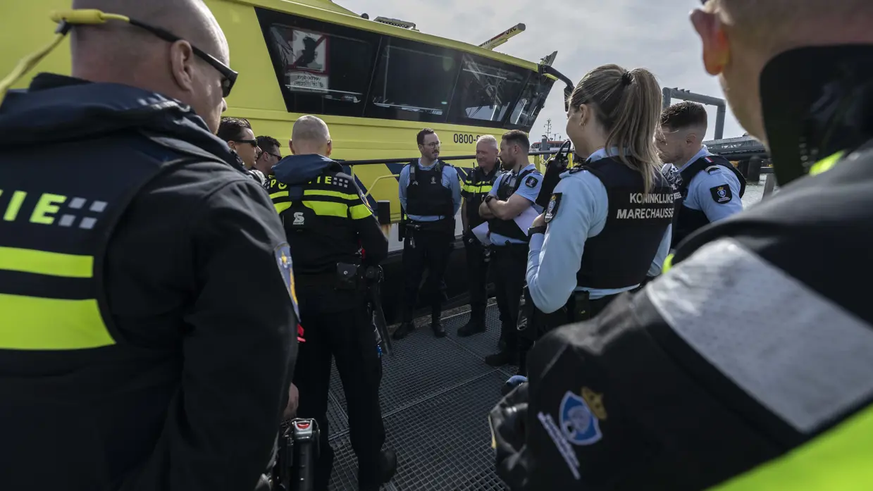 Marechaussees en politiemensen praten met elkaar op het dek van een schip.
