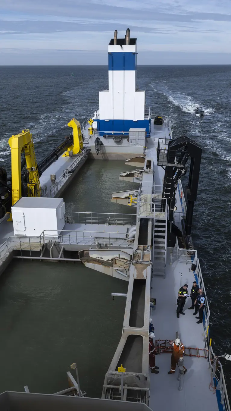 Een politieboot en een rhib-boot van de Koninklijke Marechaussee flankeren een groot schip.