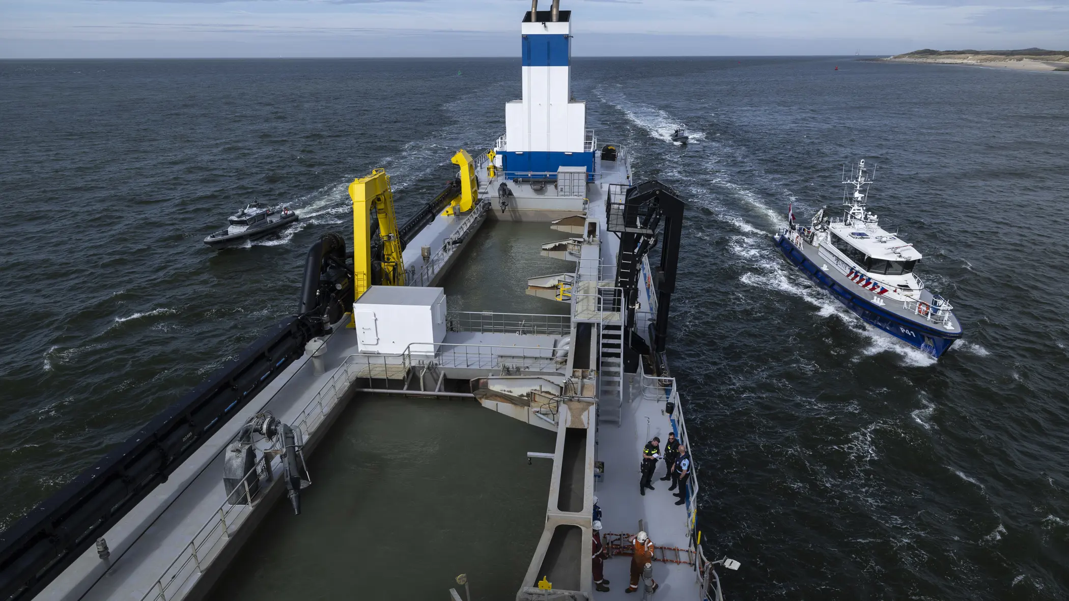 Een politieboot en een rhib-boot van de Koninklijke Marechaussee flankeren een groot schip.
