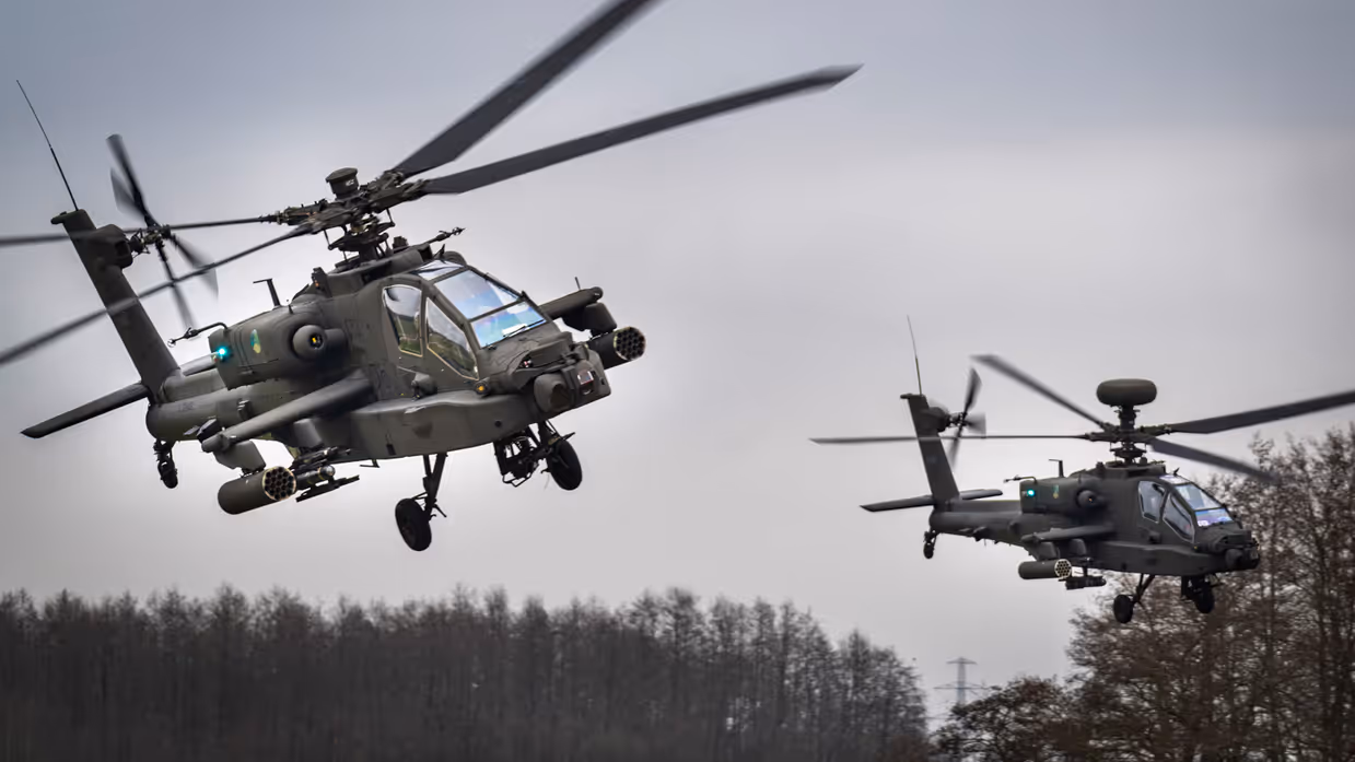 Twee Apache-helikopters vliegen door de lucht naast elkaar.