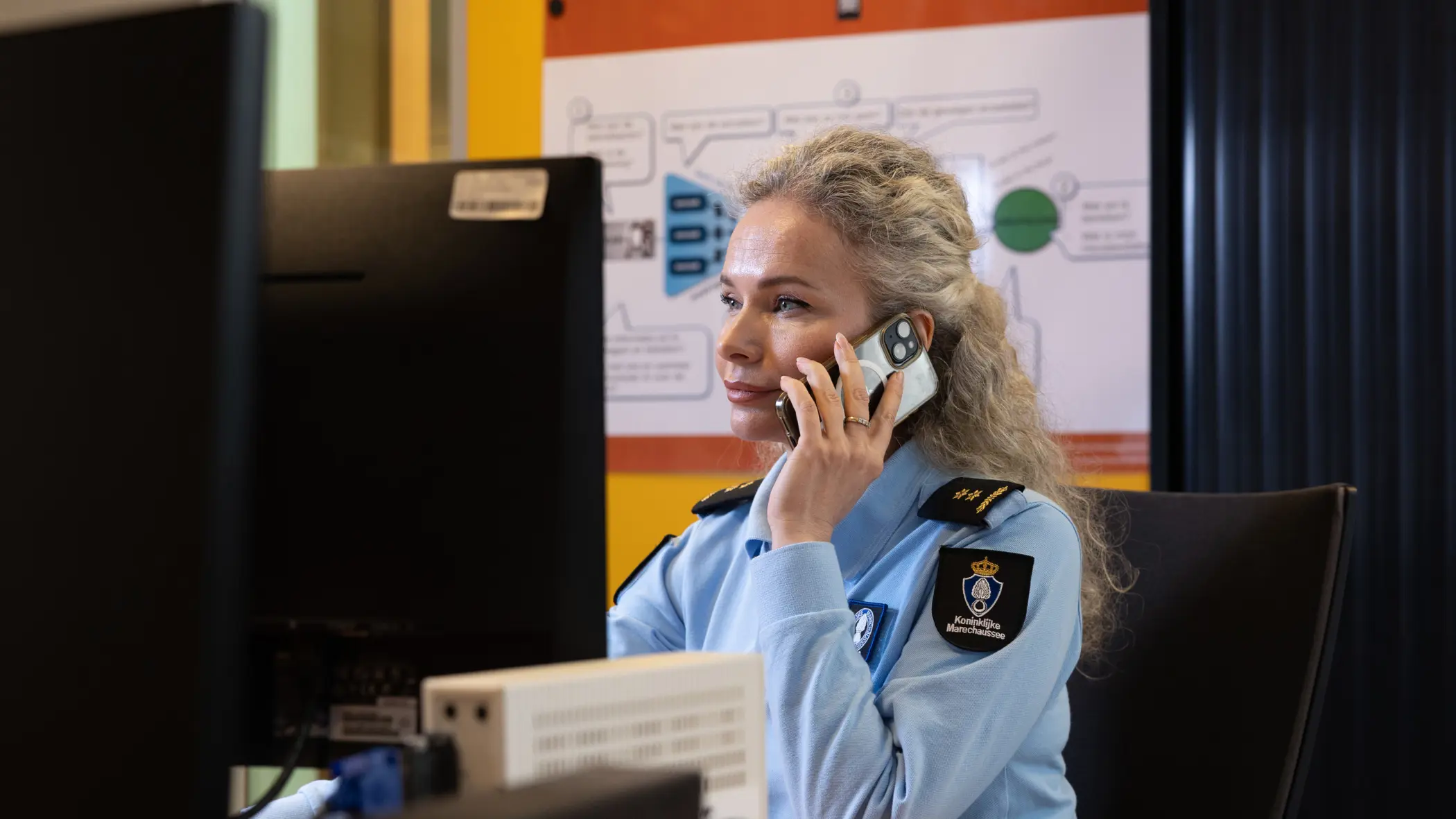 Luitenant-kolonel Irena zit achter een computer en houdt een telefoon bij haar oor.