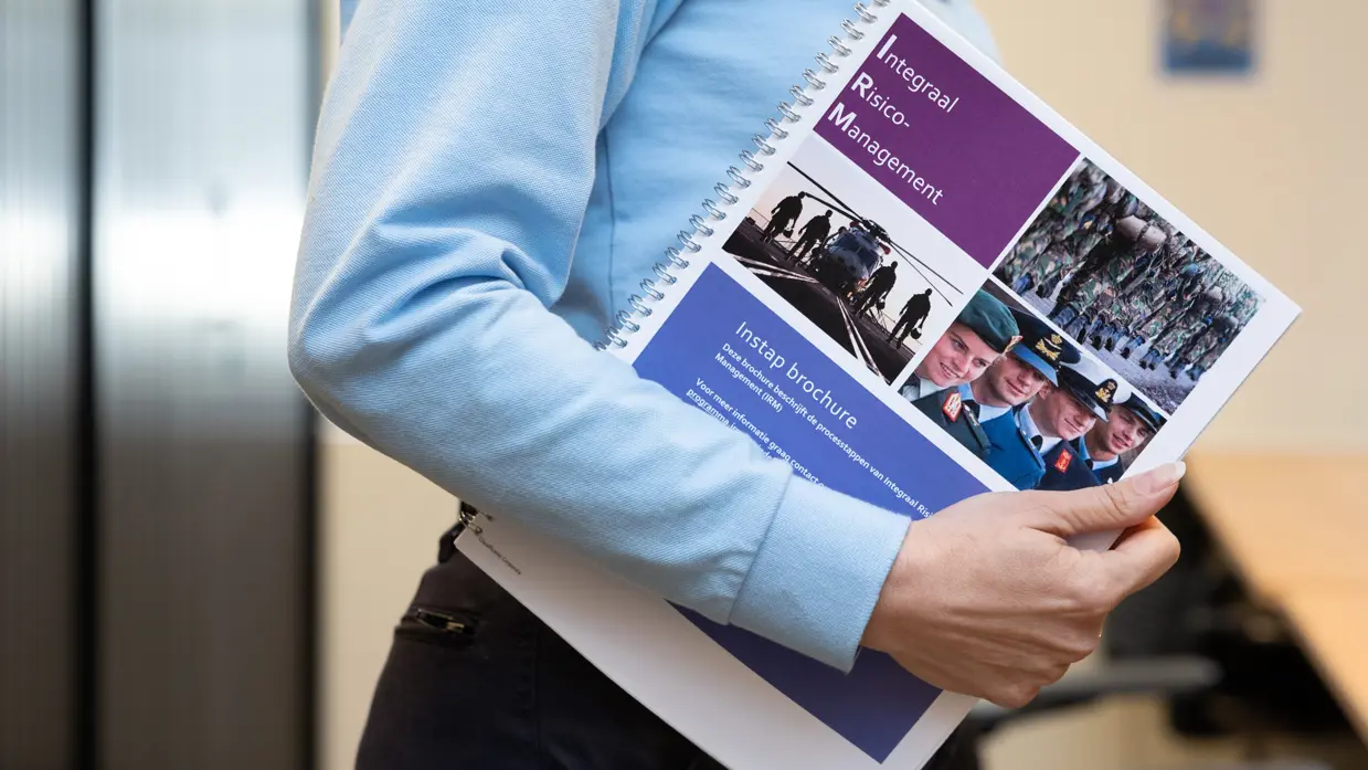 Irena van de zijkant gezien, terwijl ze een folder over Integraal Risicomanagement vasthoudt onder haar arm.