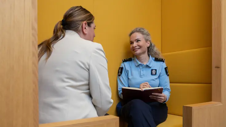 Irena zit in een gele meubelhoek en praat met een collega.