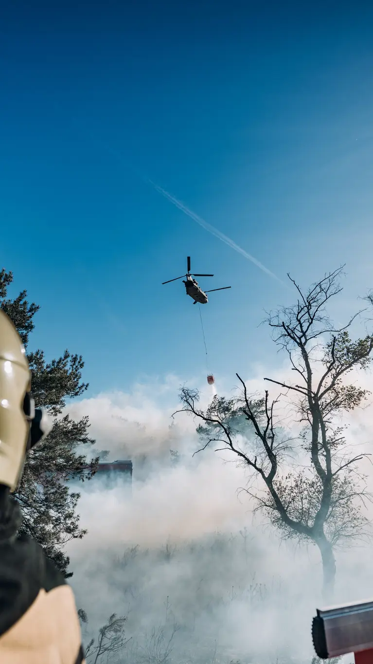 Brandweer blust brand terwijl in de lucht een Chinook-blushelikopter water dropt. 