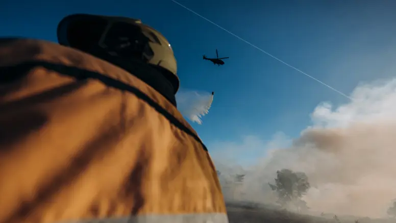 Een brandweerman kijkt omhoog en ziet hoe een helikopter bluswater loost op een brandhaard. 