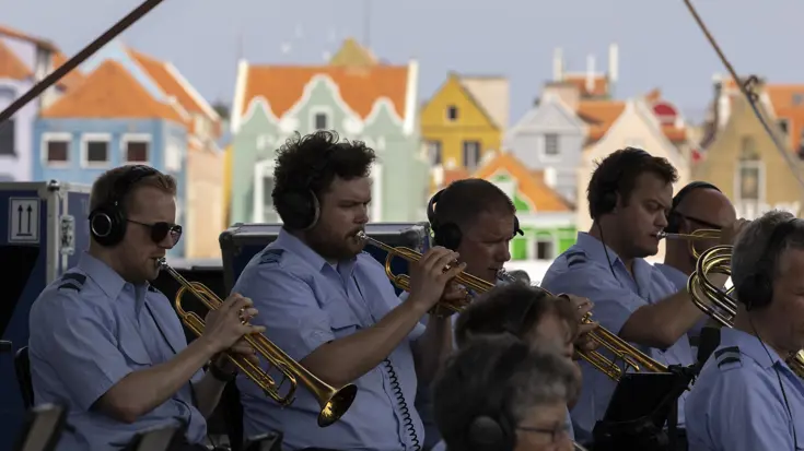 Orkestleden op blaasinstrumenten met op de achtergrond kleurrijke huizen. 