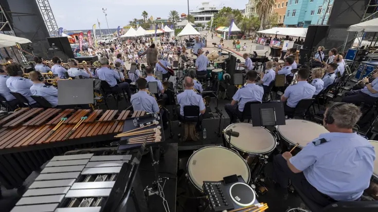 Podium vol muzikanten en publiek met uitzicht op zee. 