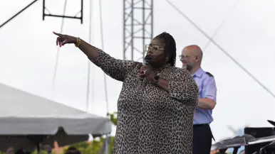 Donkere bebrilde zangeres zingt op podium en wijst naar publiek. 