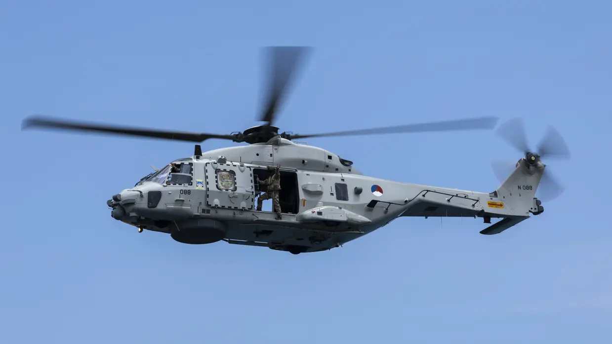 Een draaiende helikopter met bemanningslid in de deuropening. 