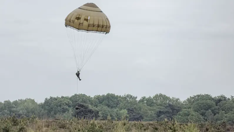 Een parachutist daalt onder een geopende parachute af boven de heide.  