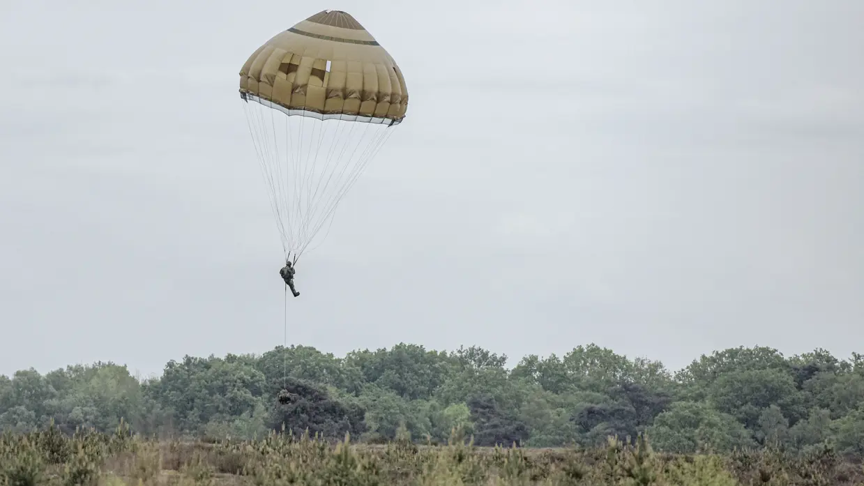 Een parachutist daalt onder een geopende parachute af boven de heide.  