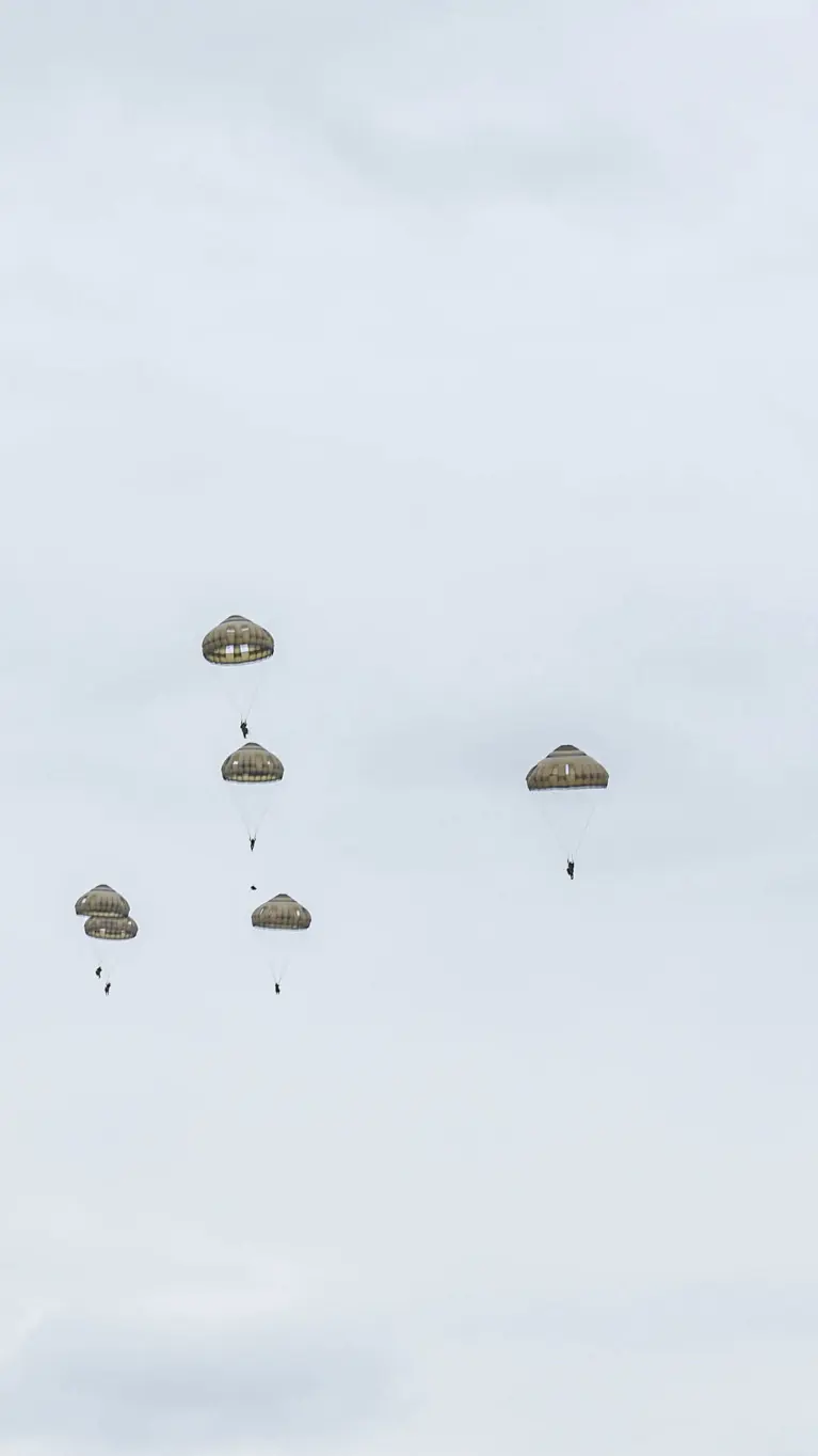 Parachutisten dalen met geopende parachutes neer boven de Belgische heide tijdens oefening Versatile Guard 