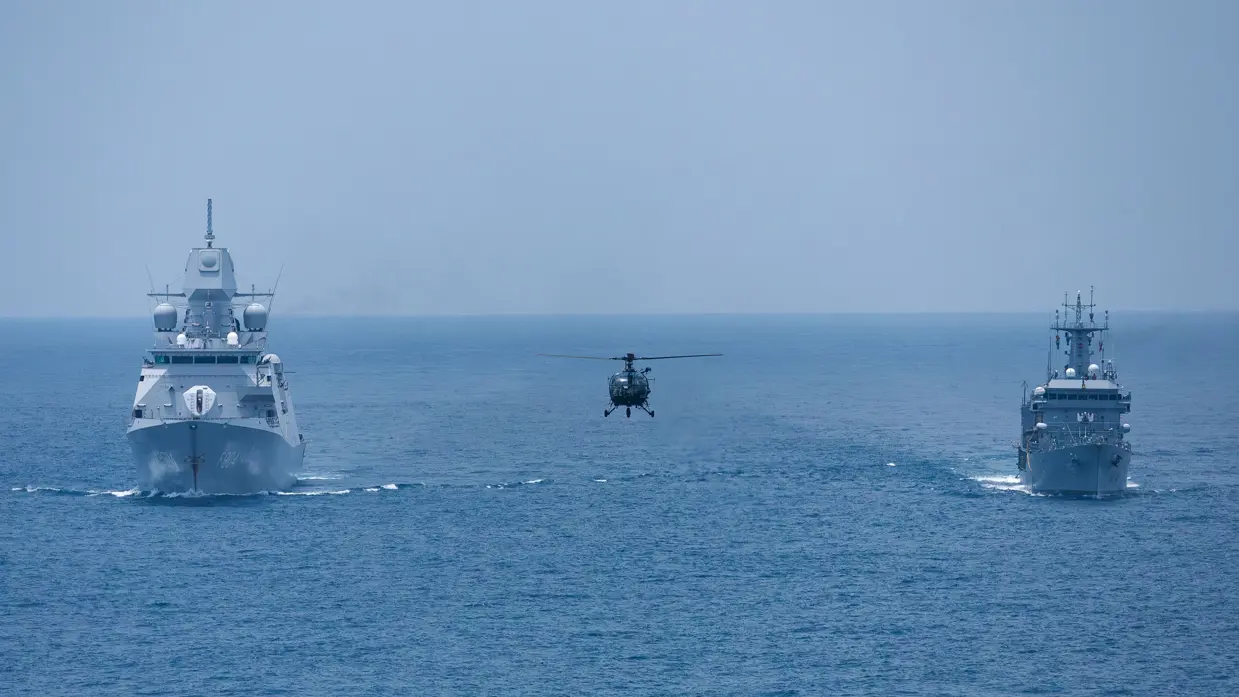 Twee schepen varen naast elkaar, een helikopter vliegt tussen ze in.