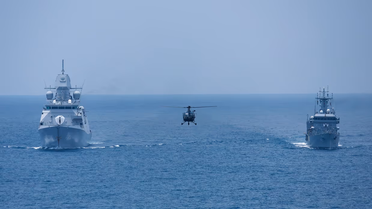Twee schepen varen naast elkaar, een helikopter vliegt tussen ze in.