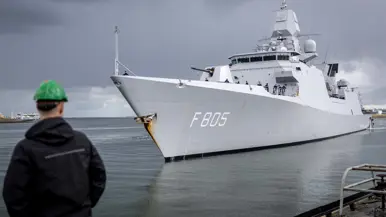 Linkerfoto: twee sleepboten escorteren de Evertsen. Rechterfoto: een marineman hoe de Evertsen richting de kade vaart. 