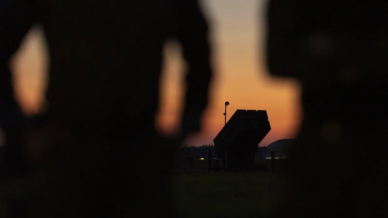 Het silhouette van het luchtafweersysteem is zichtbaar op de horizon tussen twee militairen in die op de voorgrond staan.