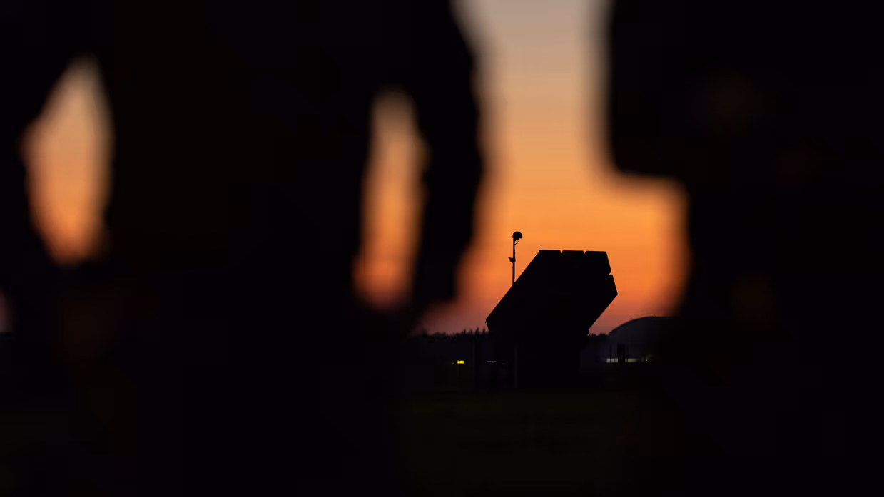Het silhouette van het luchtafweersysteem is zichtbaar op de horizon tussen twee militairen in die op de voorgrond staan.