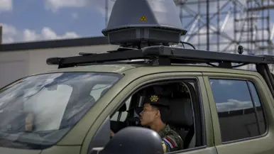 Twee militairen zitten in een voertuig met een grijze bol op het dak. 