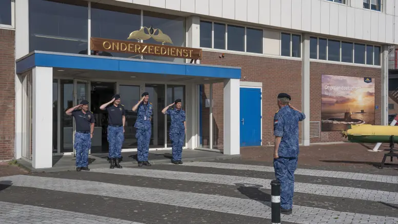  4 marinemensen staan in houding voor een hoge militair. 