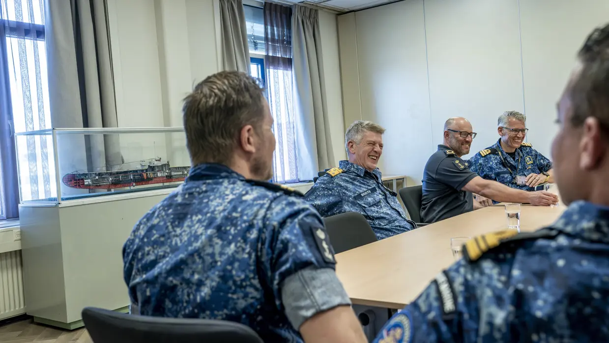 5 marinemensen zitten lachend met elkaar aan tafel. 