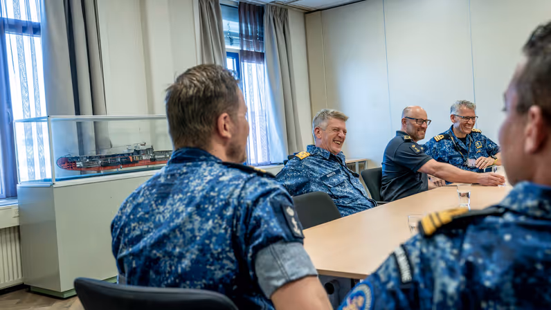 5 marinemensen zitten lachend met elkaar aan tafel. 