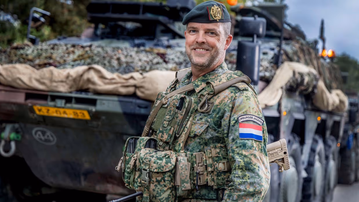 Een militair poseert voor een militaire truck.