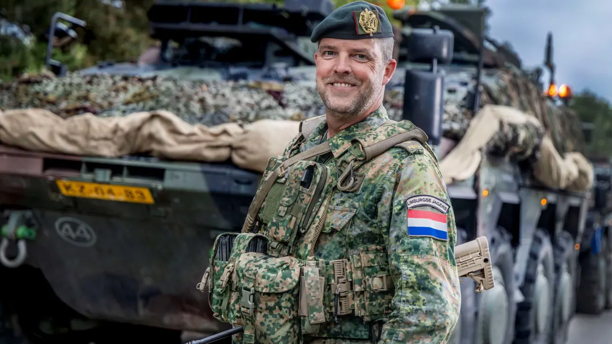 Een militair poseert voor een militaire truck.
