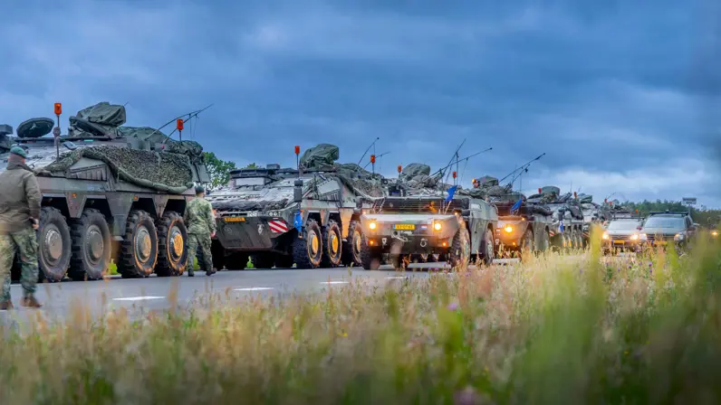 Militaire voertuigen staan opgesteld langs een weg onder een donkere lucht. 