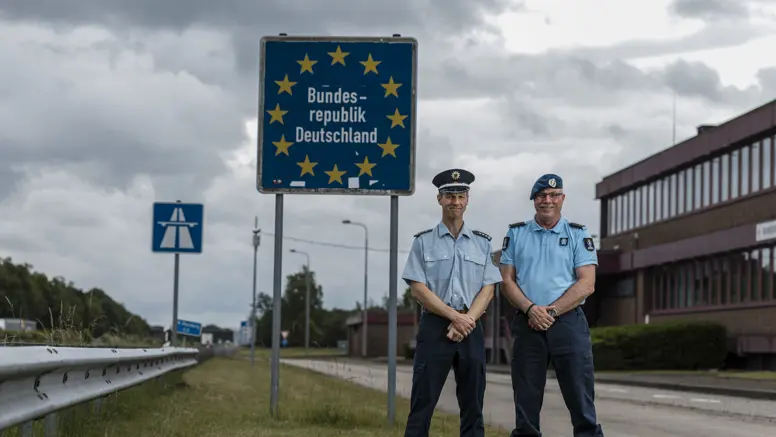 Eerste luitenant Herman en zijn Duitse evenknie voor een grensbord langs de snelweg. 