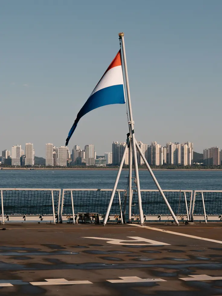 Nederlandse vlag op dek van schip met uitzicht op wolkenkrabbers.