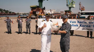  Een Nederlandse marineman in DT wordt met een bloemetje welkom geheten door een Zuid-Koreaanse collega.