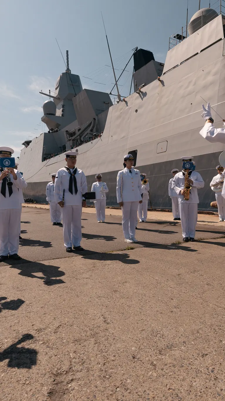 Marinemensen in DT staan met instrumenten op een kade bij een groot marineschip. 