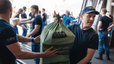 2 personen, van wie een met pet, houden een groene postzak vast. 