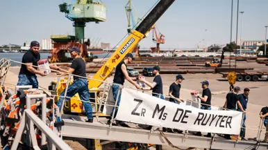 Marinemensen geven op trap marineschip een lading aan elkaar over.